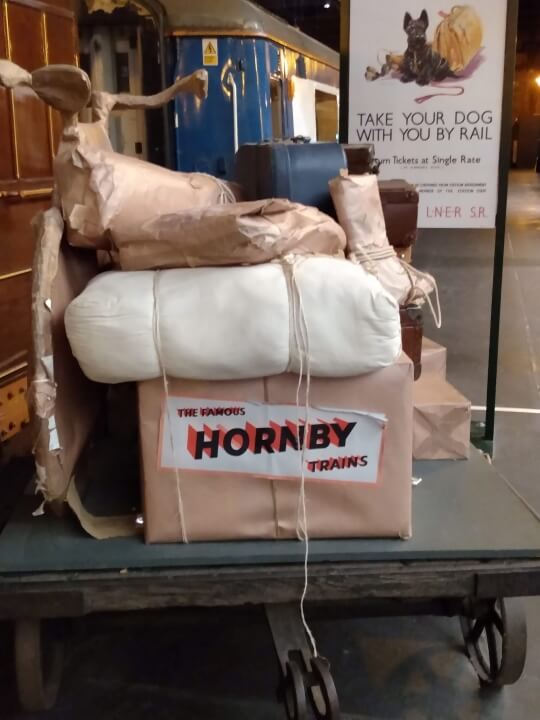A station cart piled with parcels display next to a steam train carriage at the National Railway Museum